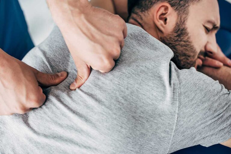 Person seated at home reviewing digestive symptoms while a clinician discusses posture and abdominal discomfort.